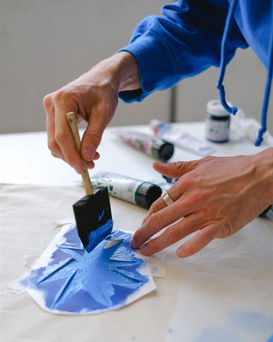 Manos aplicando pintura azul con una plantilla sobre lienzo, en un taller con luz natural